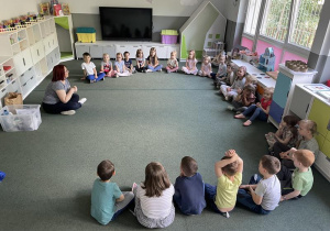 dzieci siedzą na dywanie i słuchają edukatorki